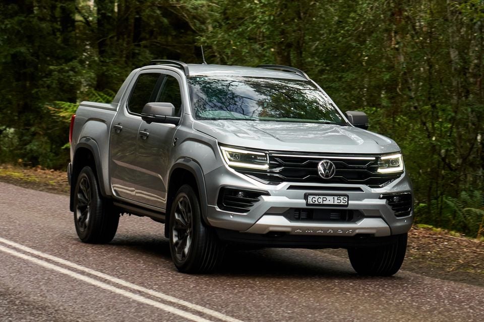A silver Volkswagen Amarok dual-cab ute seen from the front-side angle on a road surrounded by forest