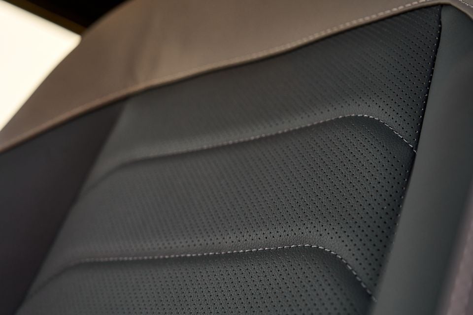 Close-up of a perforated black leather car seat with contrasting stitching detail