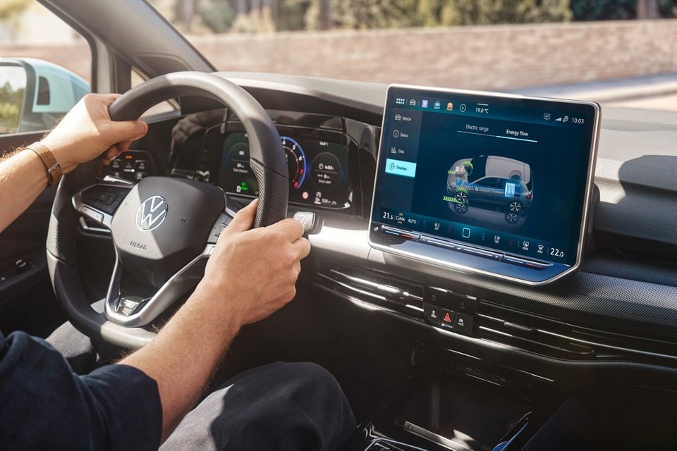 Interior of a Volkswagen Golf showing the steering wheel and large central touchscreen displaying an energy flow diagram for a hybrid powertrain