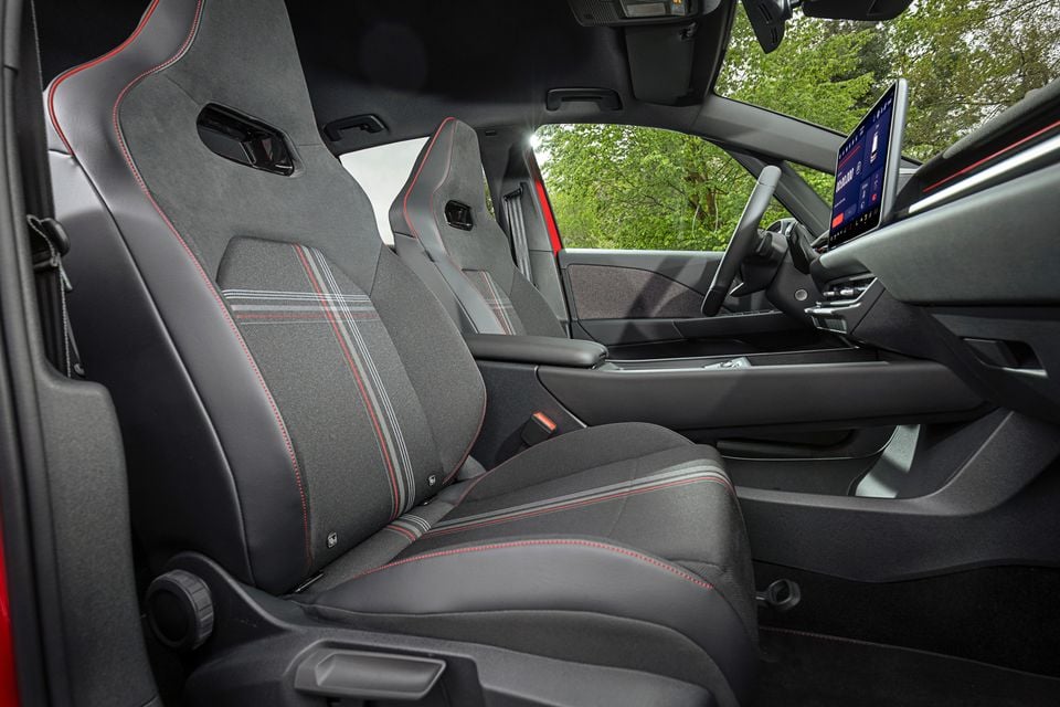 Interior of the 2027 Volkswagen ID.3 GTI showing sport front seats with red stitching and plaid fabric inserts, alongside the steering wheel and touchscreen infotainment display