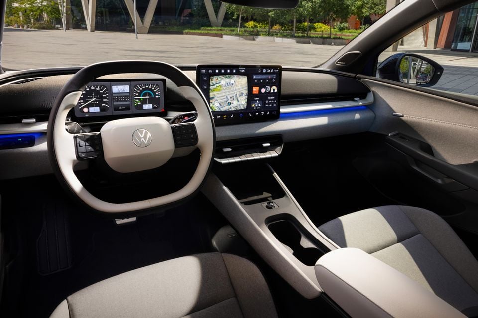 Interior of a Volkswagen ID. Polo showing the steering wheel, digital instrument cluster, large central touchscreen with navigation, and two-tone grey and white seats