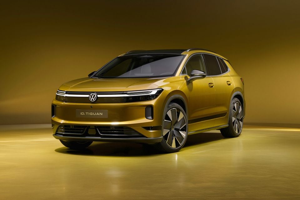 A gold 2027 Volkswagen ID. Tiguan electric SUV shown from the front left in a studio with a matching gold backdrop