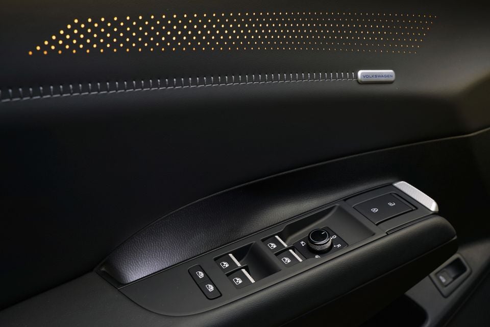 Driver's door panel in the 2027 Volkswagen ID. Tiguan with window and mirror switches, contrast stitching and backlit perforated speaker grille