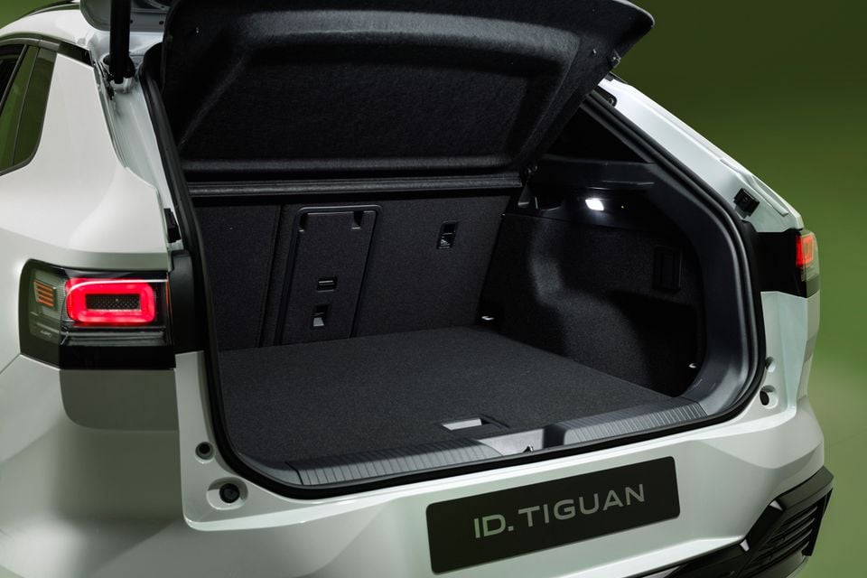 The open tailgate of a white 2027 Volkswagen ID. Tiguan reveals its carpeted boot space, seen from the rear in a studio.