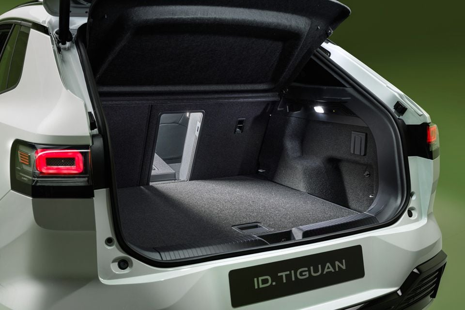 The open boot of a white 2027 Volkswagen ID. Tiguan SUV, showing a carpeted cargo area with a ski pass-through and a lit interior.