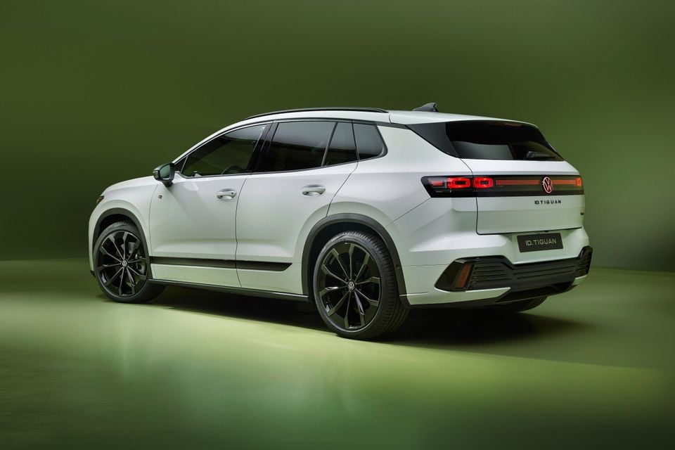 A white 2027 Volkswagen ID. Tiguan electric SUV with black wheels, seen from the rear quarter in a green-lit studio