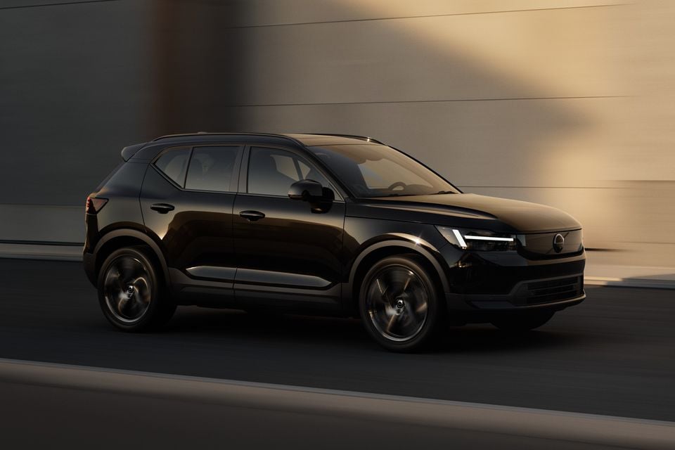 A black Volvo small SUV driving past a building, seen from the front-side angle