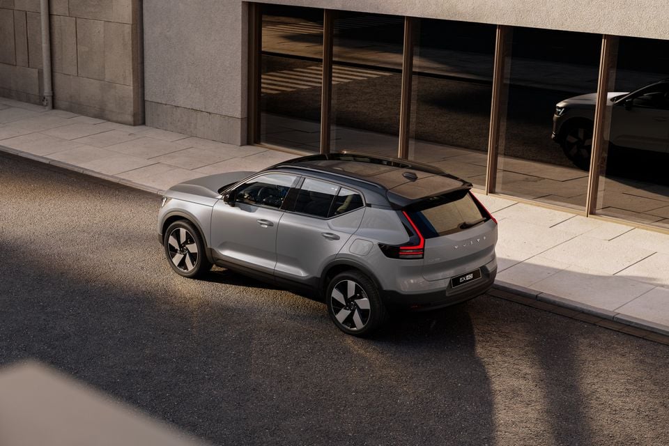 A silver Volvo EX40 SUV seen from a high rear three-quarter angle, parked beside a modern building on a city street.