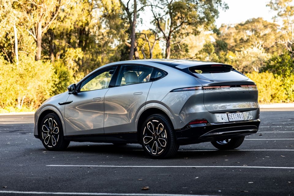A silver 2027 Xpeng G6 electric SUV parked in an empty car park, seen from the rear quarter with bushland behind