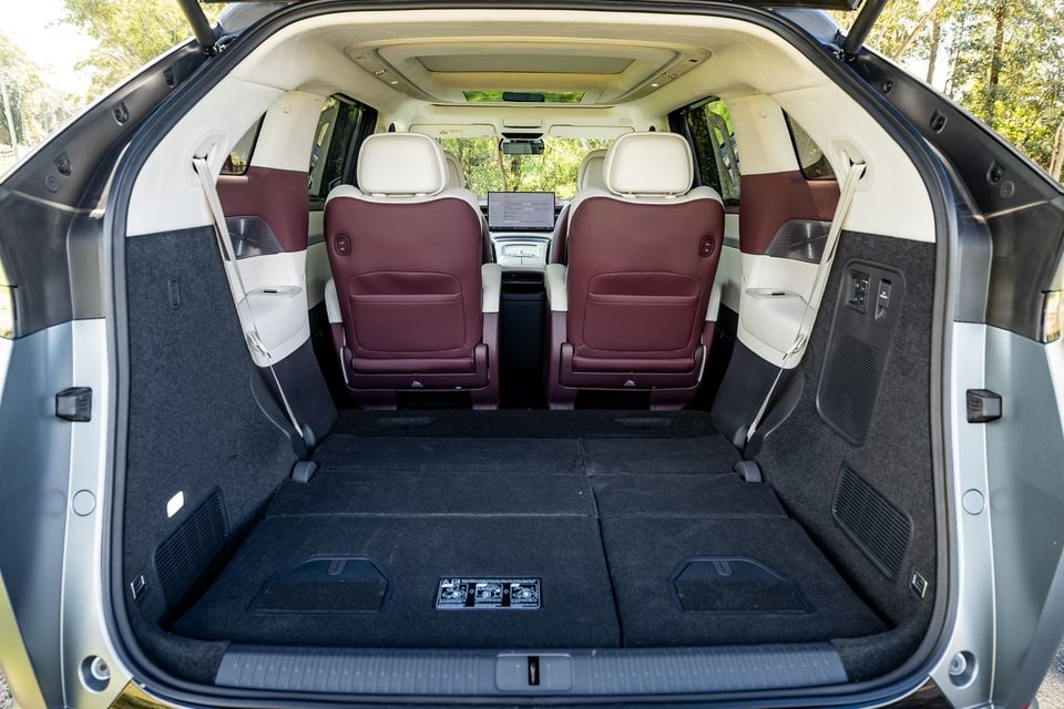 Boot space of the 2027 Xpeng X9, viewed from the rear with the tailgate open, showing a large flat cargo area and two captain's chairs in the second row with burgundy and cream leather upholstery