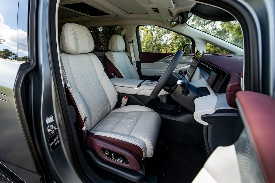 Interior view of the 2027 Xpeng X9 showing the front seats with cream and burgundy leather upholstery, a large touchscreen infotainment display, and a yoke-style steering wheel
