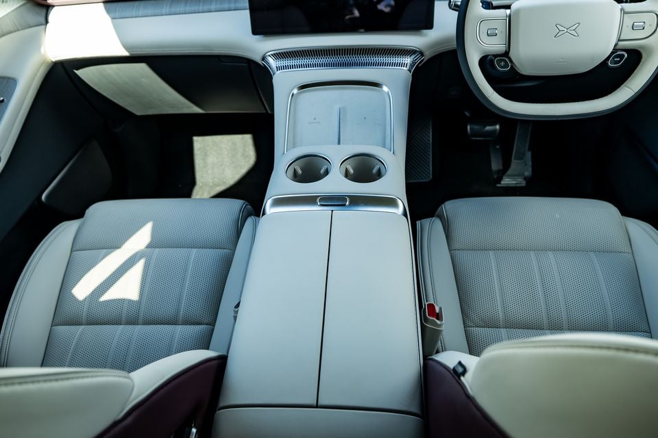 Interior view of the Xpeng X9 showing the front centre console, cup holders, armrest, and light grey perforated leather front seats