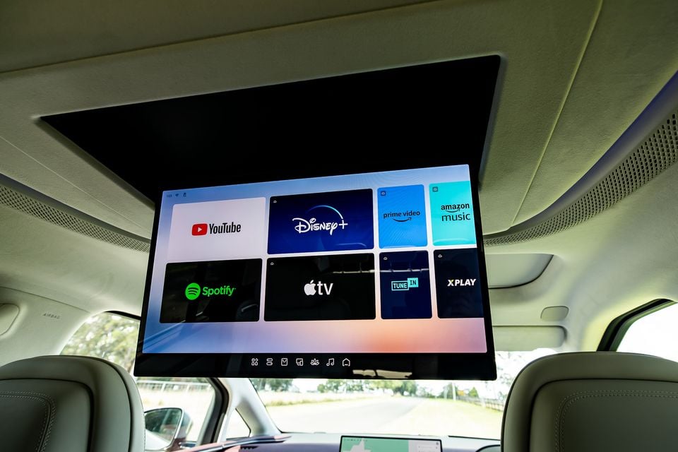 Roof-mounted rear entertainment screen in a 2027 Xpeng X9 showing streaming apps including YouTube, Disney+, Prime Video, Amazon Music, Spotify, Apple TV, TuneIn and Xplay