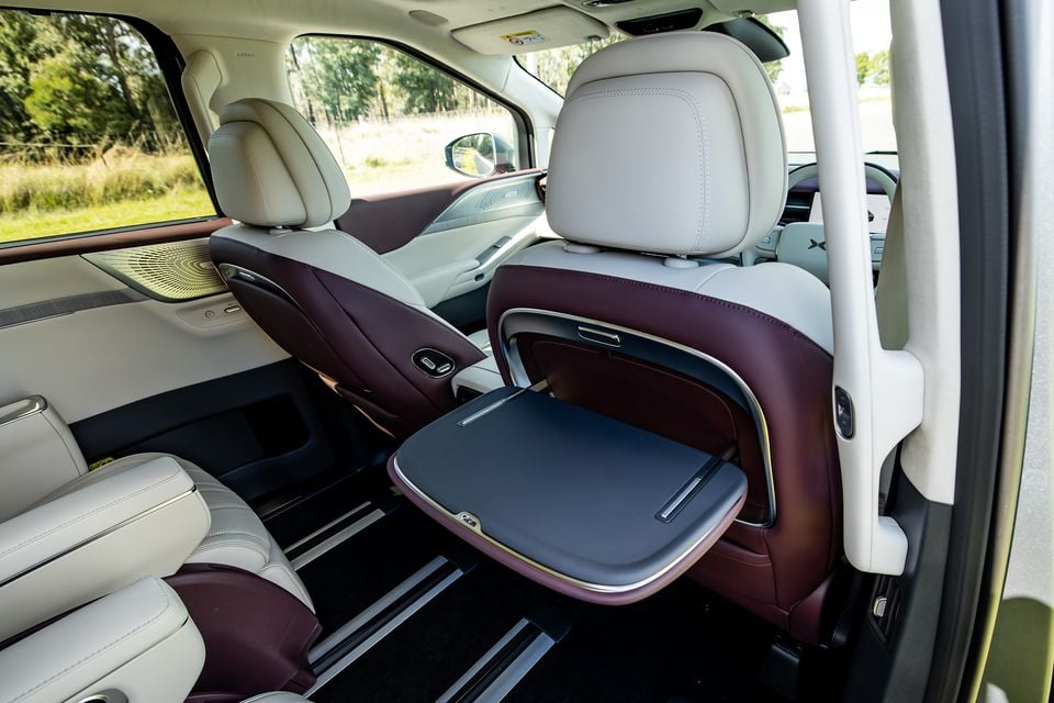 Rear passenger cabin of the 2027 Xpeng X9 showing luxurious two-tone cream and burgundy leather captain's chairs with a fold-out tray table extended from the front seatback