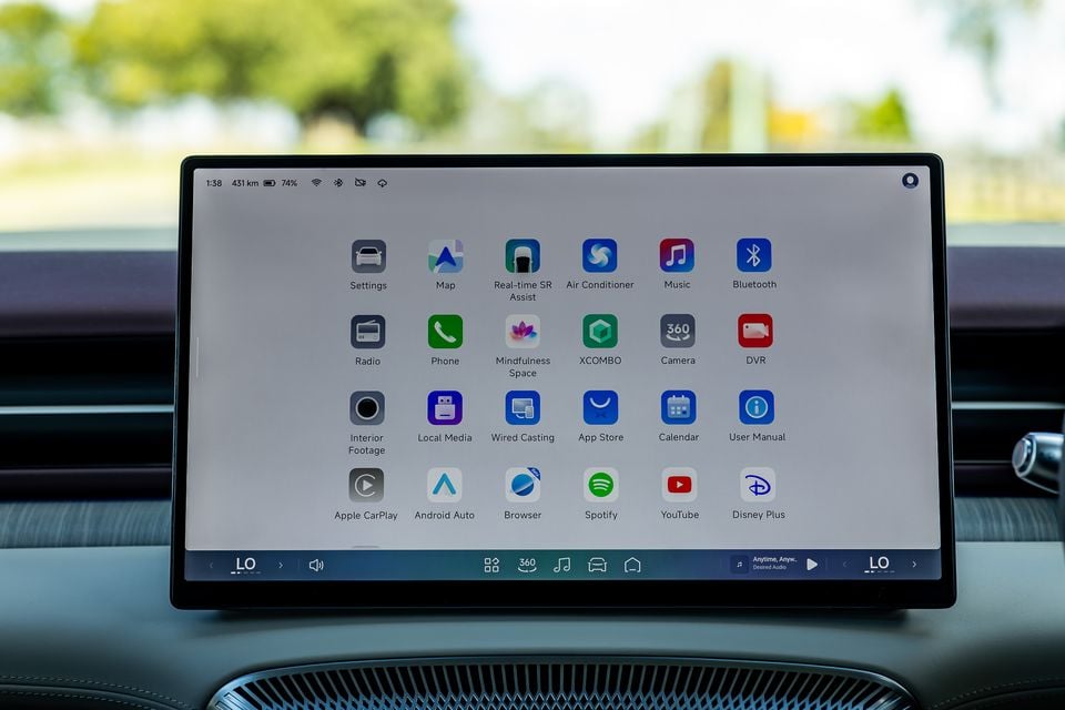 The infotainment touchscreen of a 2027 Xpeng X9 showing a home screen with app icons including Apple CarPlay, Android Auto, Spotify, YouTube, Disney Plus, and various vehicle controls