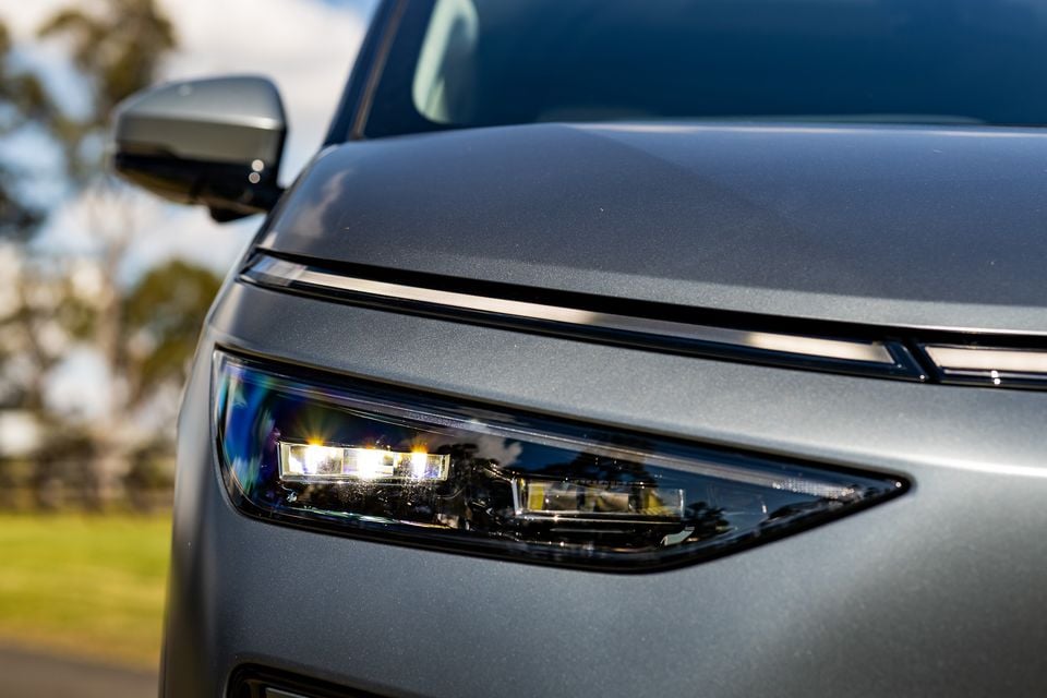 Close-up of the LED headlight on a silver XPENG X9, showing the illuminated light cluster and bonnet detail