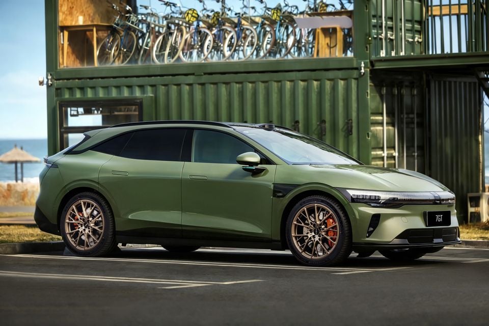 A green Zeekr 7GT shooting brake parked near a coastal area with a bicycle storage structure in the background, seen from the front-side angle.