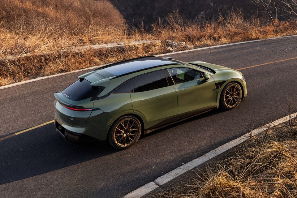 A green Zeekr 7GT seen from above and behind on a winding road, showing its sleek fastback roofline and gold alloy wheels
