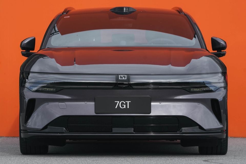 Front view of a Zeekr 7GT in dark grey, photographed against an orange background