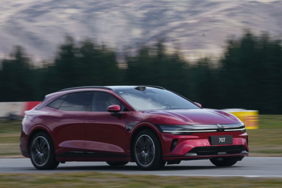 A red Zeekr 7GT hatchback driving on a race track with mountains and trees in the background