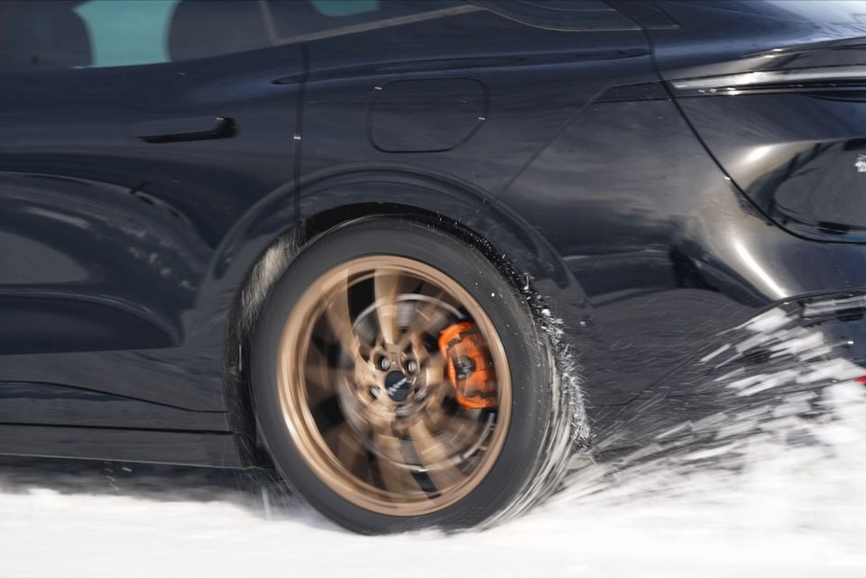Close-up of a spinning bronze alloy wheel with orange brake caliper on a black Zeekr 7GT driving through snow
