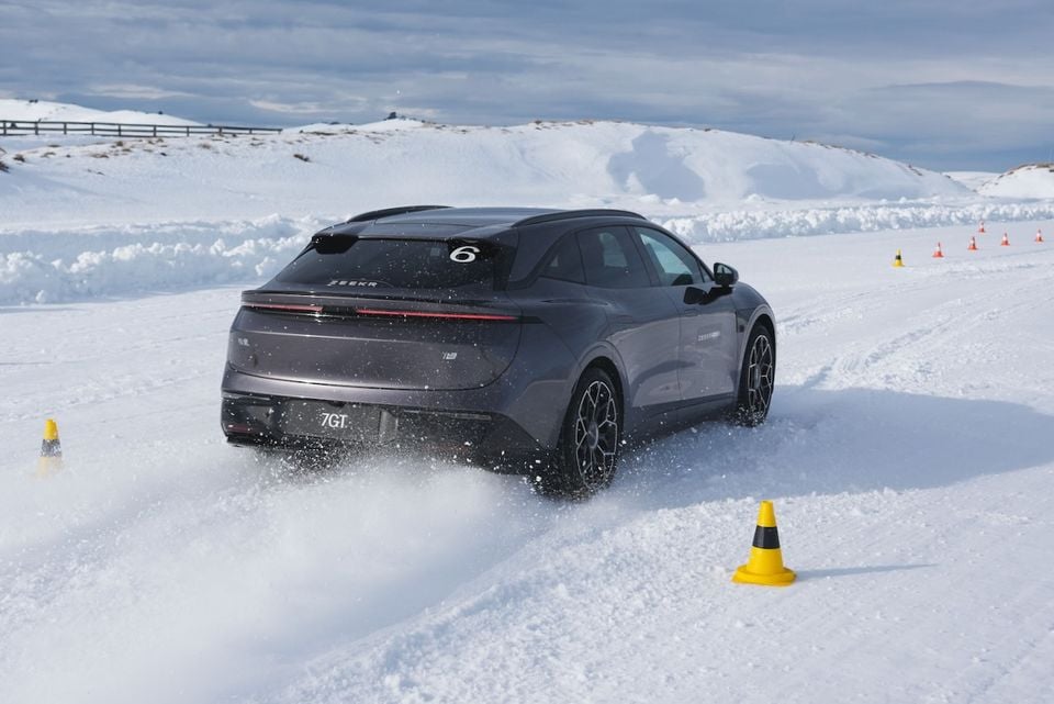 A grey Zeekr 7GT SUV being driven through a snow course with cones, seen from the rear three-quarter angle, spraying snow as it corners.