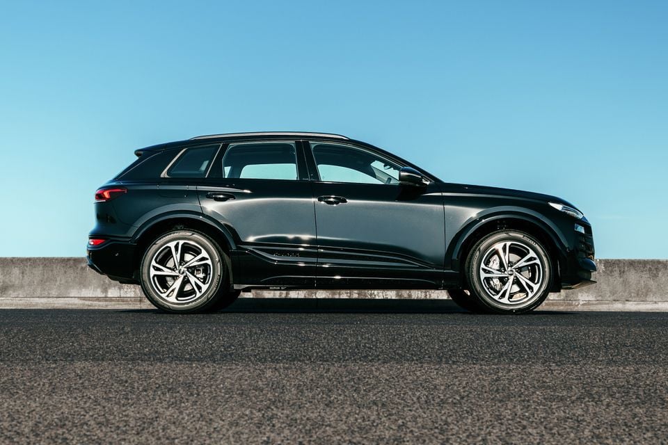 A black Audi Q6 e-tron SUV seen from the side, parked on an open road against a clear blue sky.