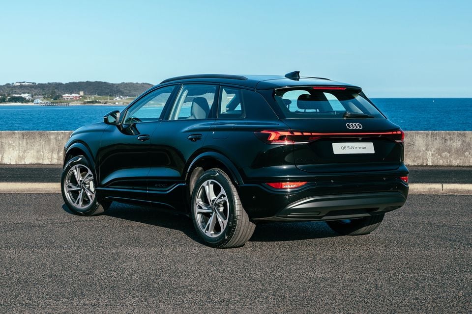 A black Audi Q6 SUV e-tron seen from the rear three-quarter angle, parked near a waterfront on a sunny day.