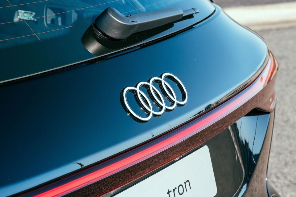 Close-up of the Audi four-ring badge on the rear of an Audi Q6 e-tron, showing the tail light strip and rear wiper