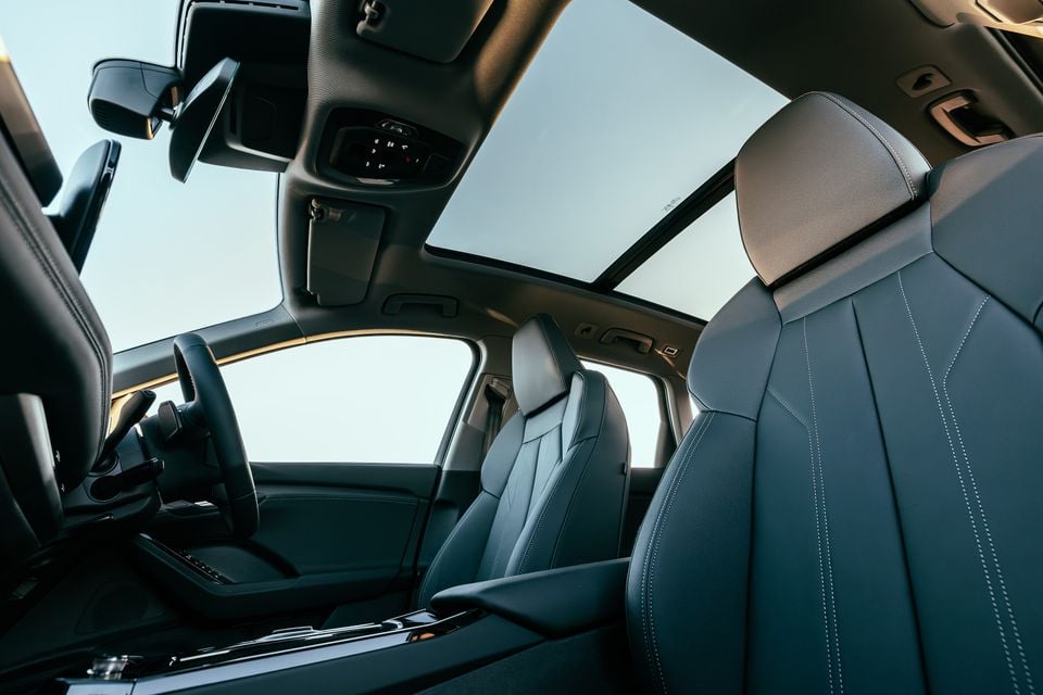 Interior of a 2027 Audi Q6 e-tron showing dark leather front seats with contrast stitching, a panoramic sunroof, and steering wheel