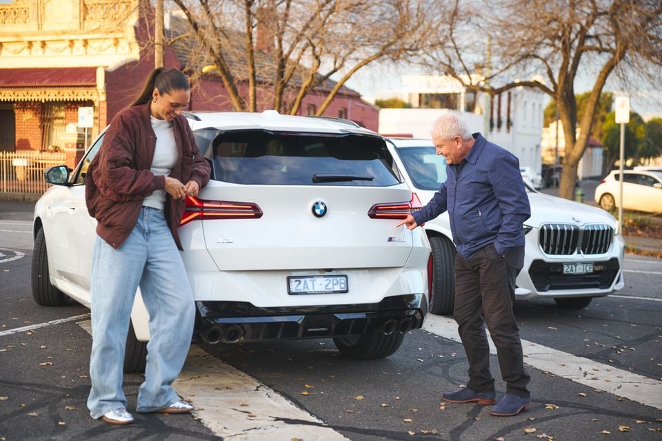 Two people standing behind a white BMW X2 M50 SUV parked on a street in Melbourne, with a white BMW X5 visible in the background