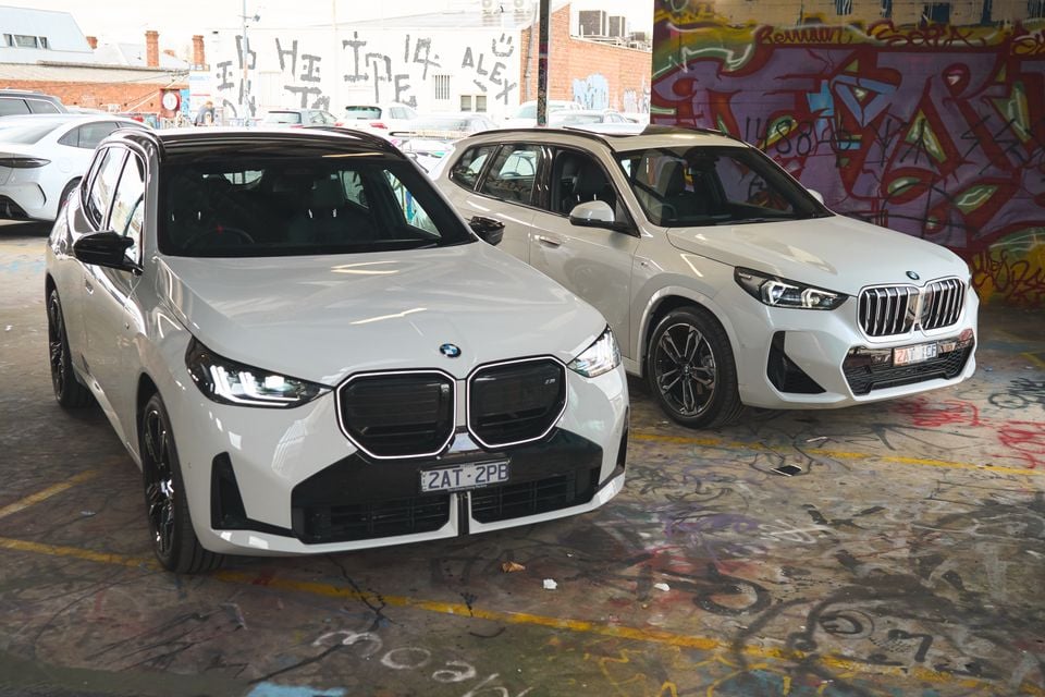 Two white BMW SUVs parked side by side in a graffiti-covered urban space, seen from the front