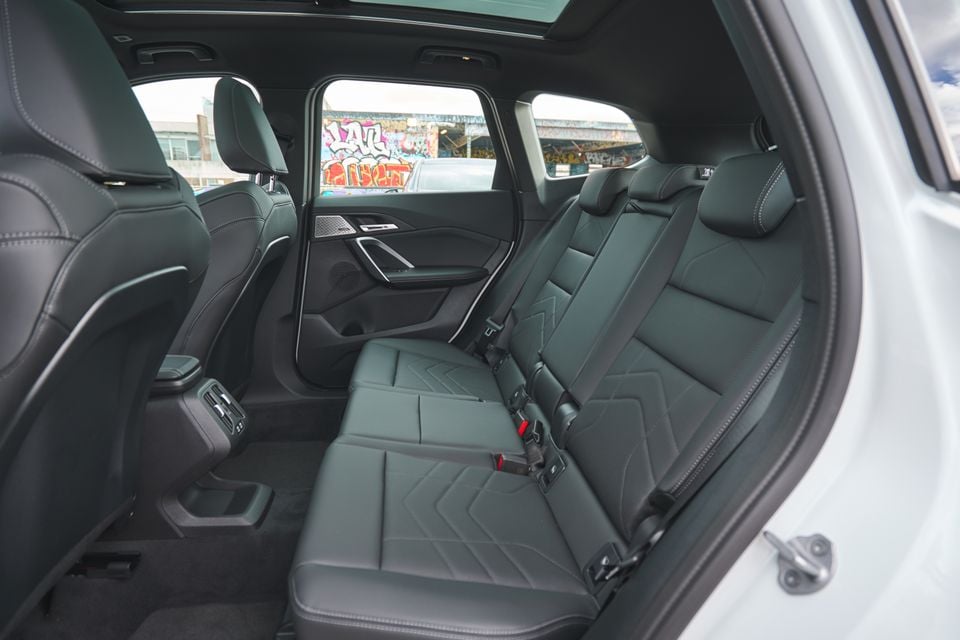 Rear seat interior of a BMW SUV showing black leather bench seat with diamond-stitch upholstery, rear climate vents, and a panoramic sunroof, with graffiti visible through the windows
