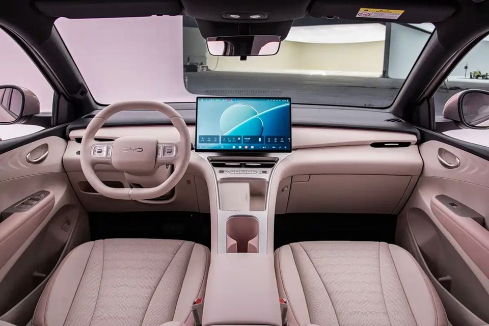 The cream-coloured interior of a BYD Atto 1 shows the steering wheel, dashboard touchscreen and front seats.