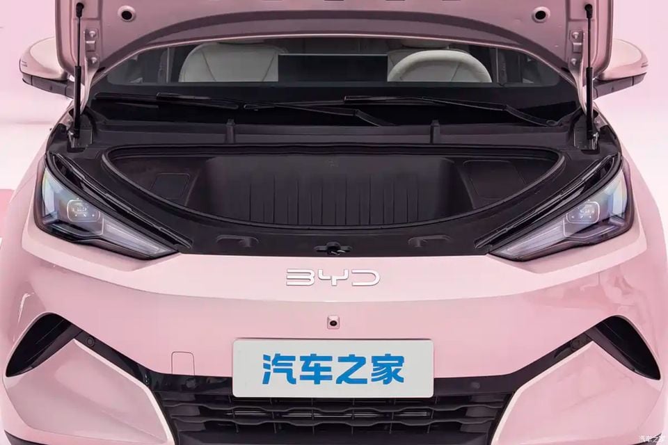 The front trunk (frunk) of a pink 2027 BYD Atto 1, viewed from the front with the storage compartment open above the headlights and badge.