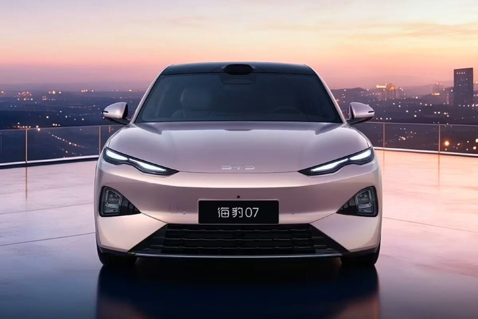 A beige BYD Seal 07 sedan photographed head-on at dusk on a rooftop with a city skyline in the background.