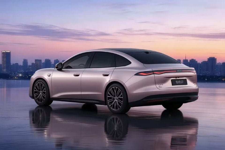 A pink BYD Seal 07 sedan photographed from the rear quarter angle with a city skyline at sunset in the background
