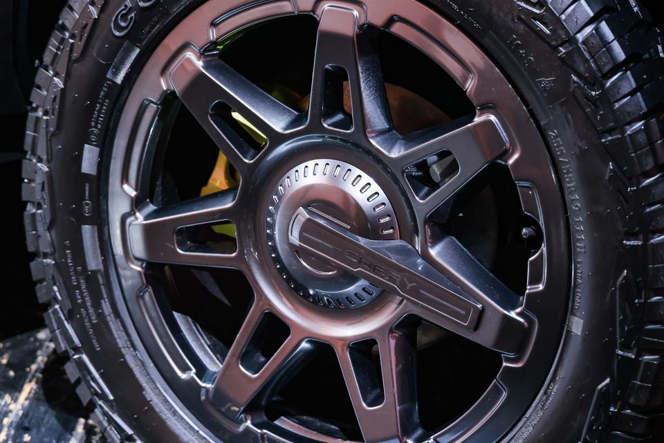 Close-up of a dark chrome five-spoke alloy wheel with Chery-branded centre cap, yellow brake caliper and all-terrain tyre on a 2027 Chery Tiggo X7