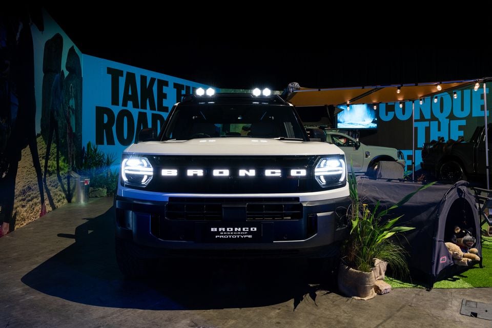 Ford Bronco Basecamp Prototype SUV displayed at an indoor event, seen from the front with illuminated grille lettering and roof-mounted driving lights