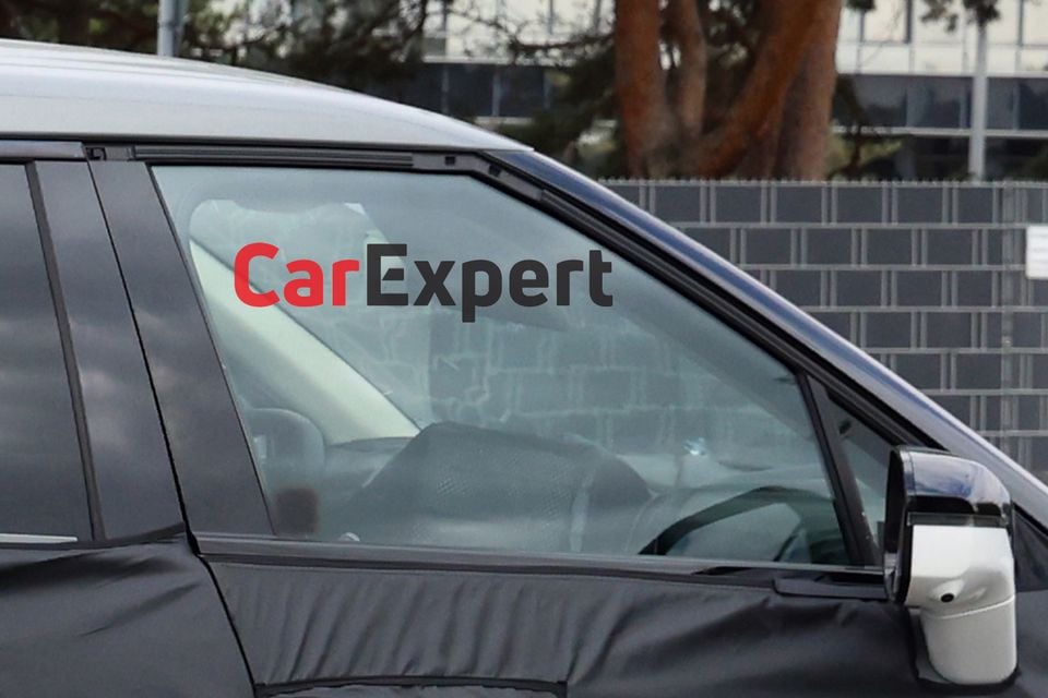 A camouflaged Kia Sportage SUV spy shot showing the side window and door area, with interior partially visible through the glass