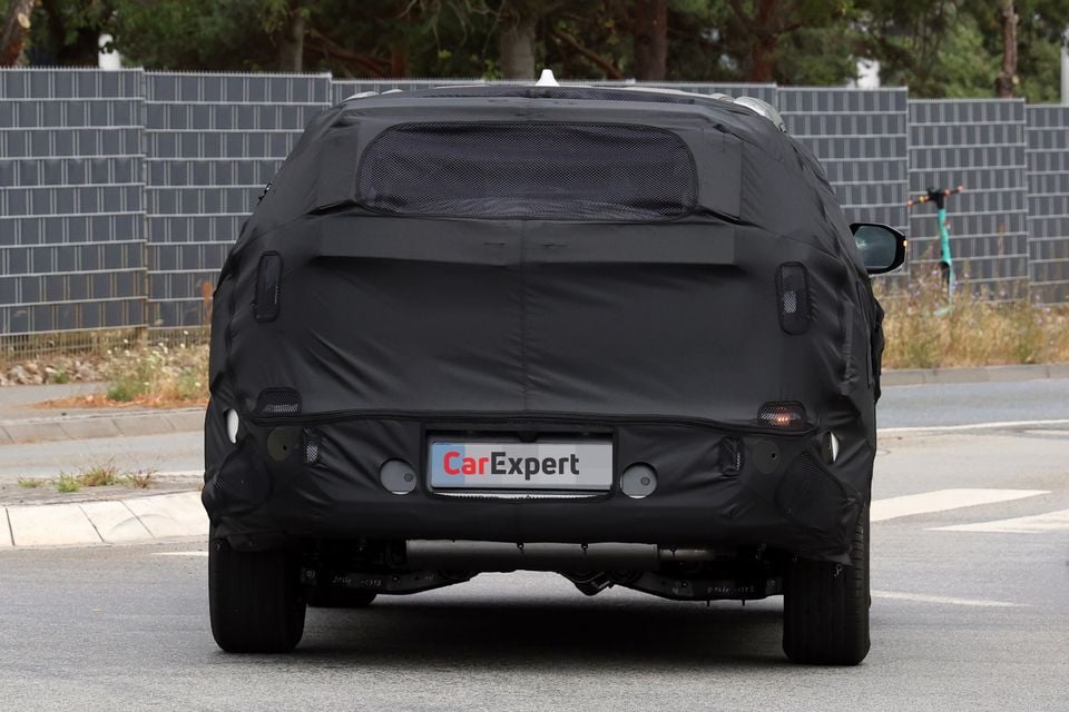 Rear view of a camouflaged Kia Sportage prototype on a public road during spy testing