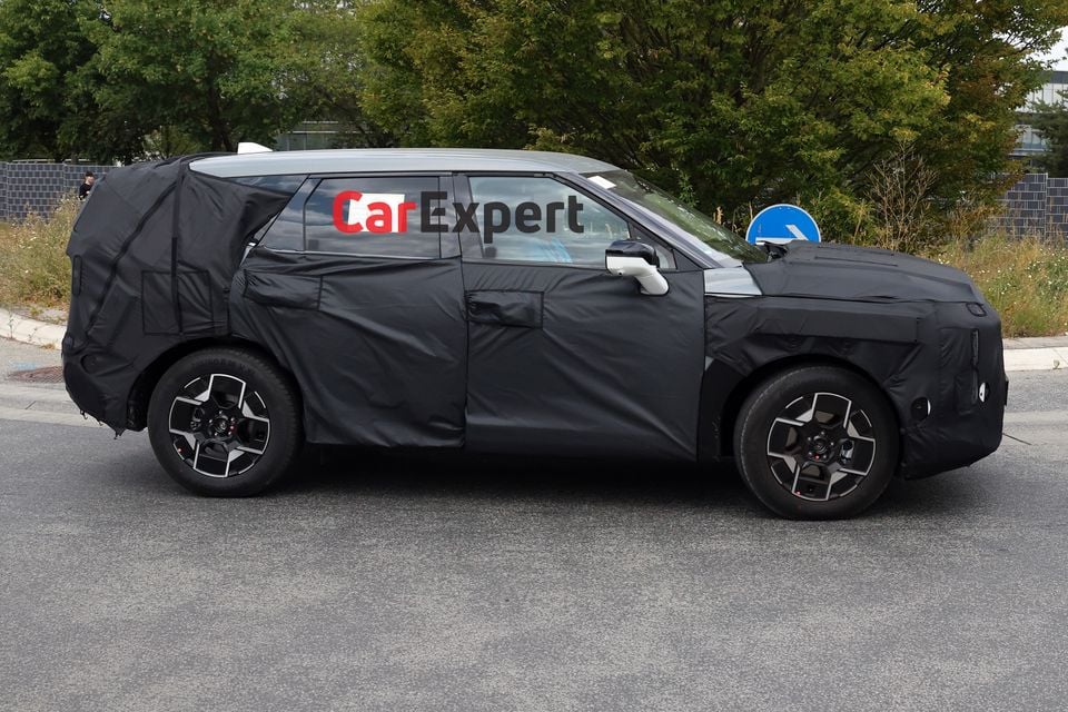 A camouflaged Kia Sportage SUV prototype seen from the side during road testing