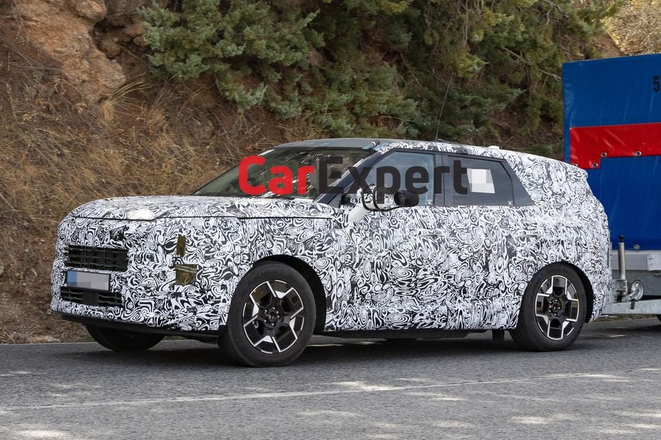 A camouflaged Kia Sportage SUV prototype seen from the front-side during road testing, with spy wrap concealing its design details