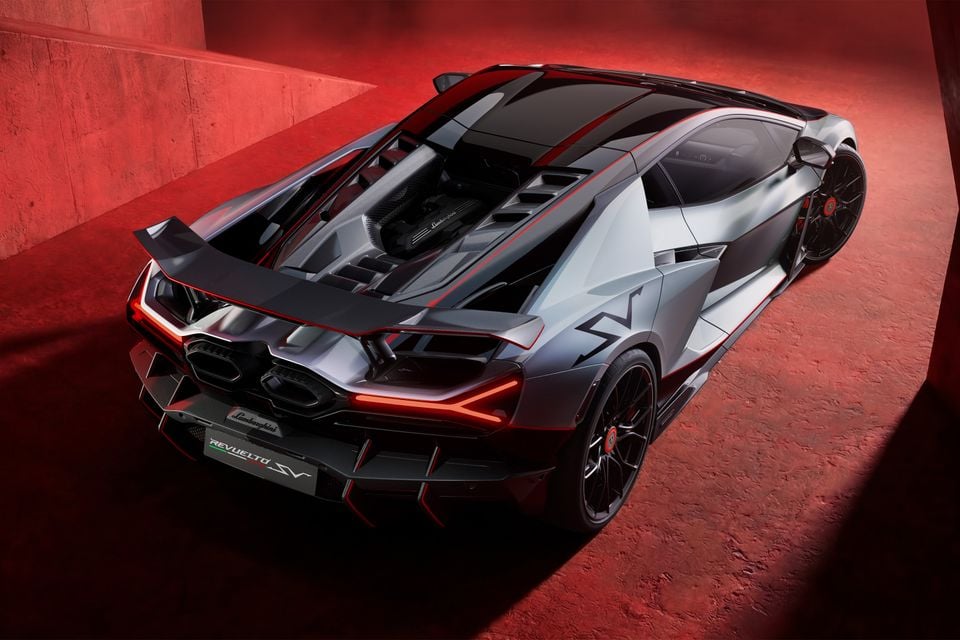 Lamborghini Revuelto SV supercar seen from a high rear three-quarter angle, showing its aggressive aerodynamic bodywork, large rear wing, twin exhausts, and red accent lighting in a red-lit studio setting.