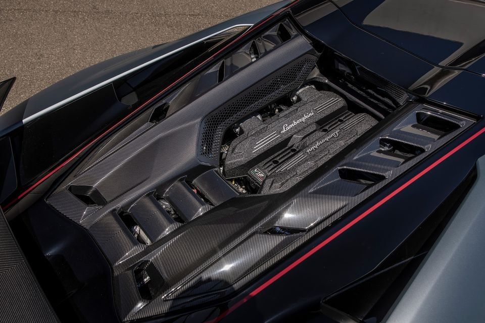 The mid-mounted Lamborghini V12 engine of a Revuelto SV, surrounded by exposed carbon fibre bodywork with red accents, viewed from above.