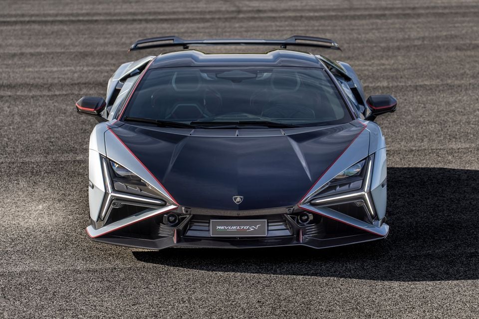 A Lamborghini Revuelto SV supercar seen from the front, parked on a racetrack surface, showing aggressive angular bodywork with red accents and a large rear wing.