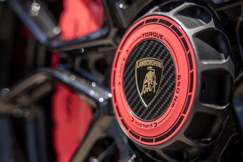 Close-up of a Lamborghini Revuelto SV wheel centre cap featuring the Lamborghini bull badge on a carbon fibre background with a red ring and torque specification markings, with a red brake calliper visible behind the dark alloy wheel spokes.