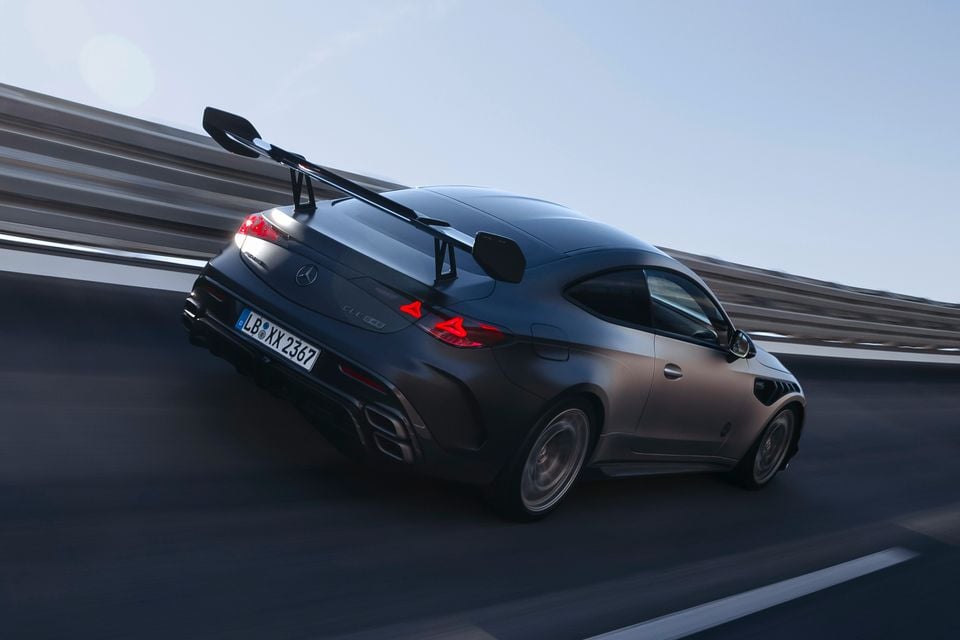 A dark matte Mercedes-AMG CLE coupe seen from the rear three-quarter angle, driving on a track with a large swan-neck rear wing fitted
