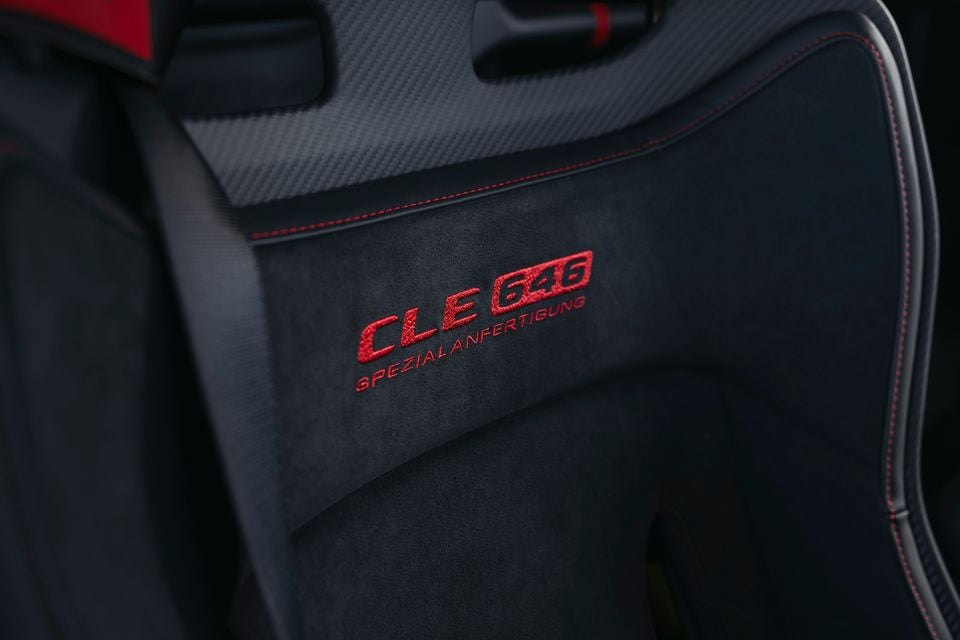 Close-up of the embroidered 'CLE 646 Spezialanfertigung' logo on a dark Alcantara seat backrest with red stitching and carbon fibre trim, inside a Mercedes-AMG CLE 646.