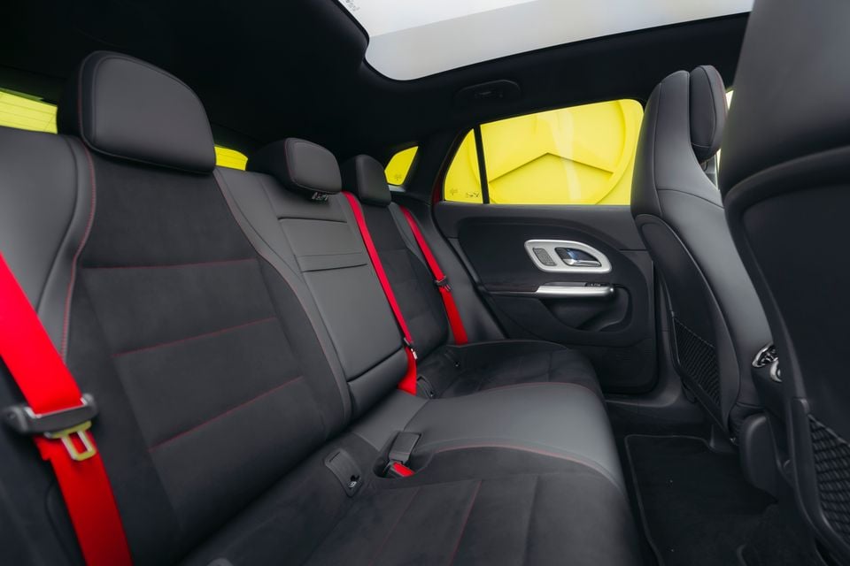 Rear seats of a Mercedes-Benz GLA featuring black upholstery with red stitching and red seatbelts, with a panoramic sunroof visible above